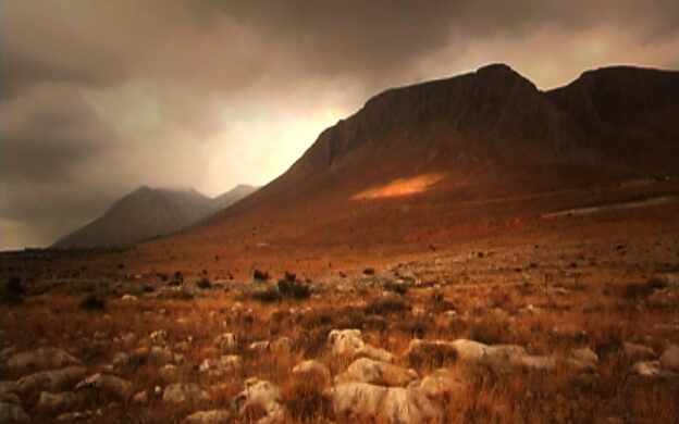 Dark orange desert mountain with dark clouds behind